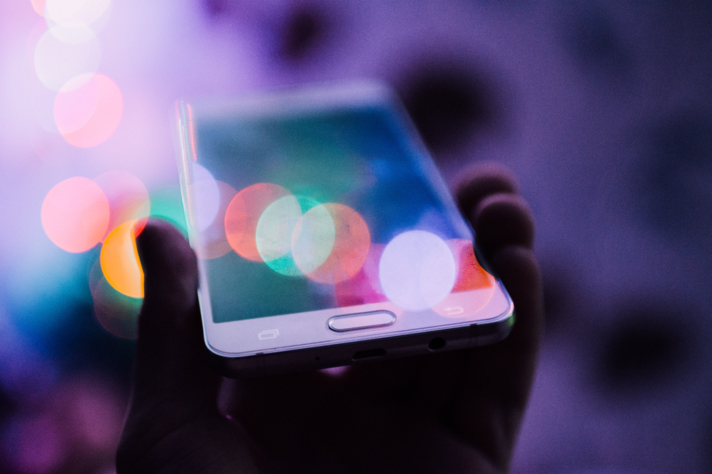a mobile cell phone held in someone's hand with the screen reflecting colorful lights