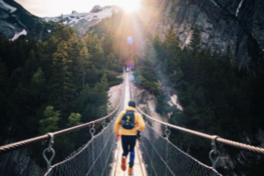 a person in active apparel on a bridge running towards a horizon of the sun meeting mountain peaks